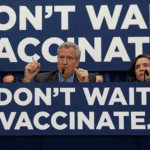 Thị trưởng Bill de Blasio trong buổi họp báo với biểu ngữ “Don’t wait. Vaccinate” (tạm dịch Đừng chần chừ. Hãy tiêm vắc xin ngay)