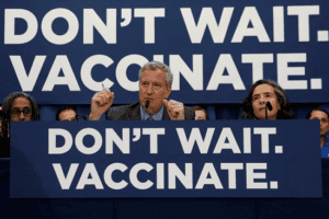 Thị trưởng Bill de Blasio trong buổi họp báo với biểu ngữ “Don’t wait. Vaccinate” (tạm dịch Đừng chần chừ. Hãy tiêm vắc xin ngay)